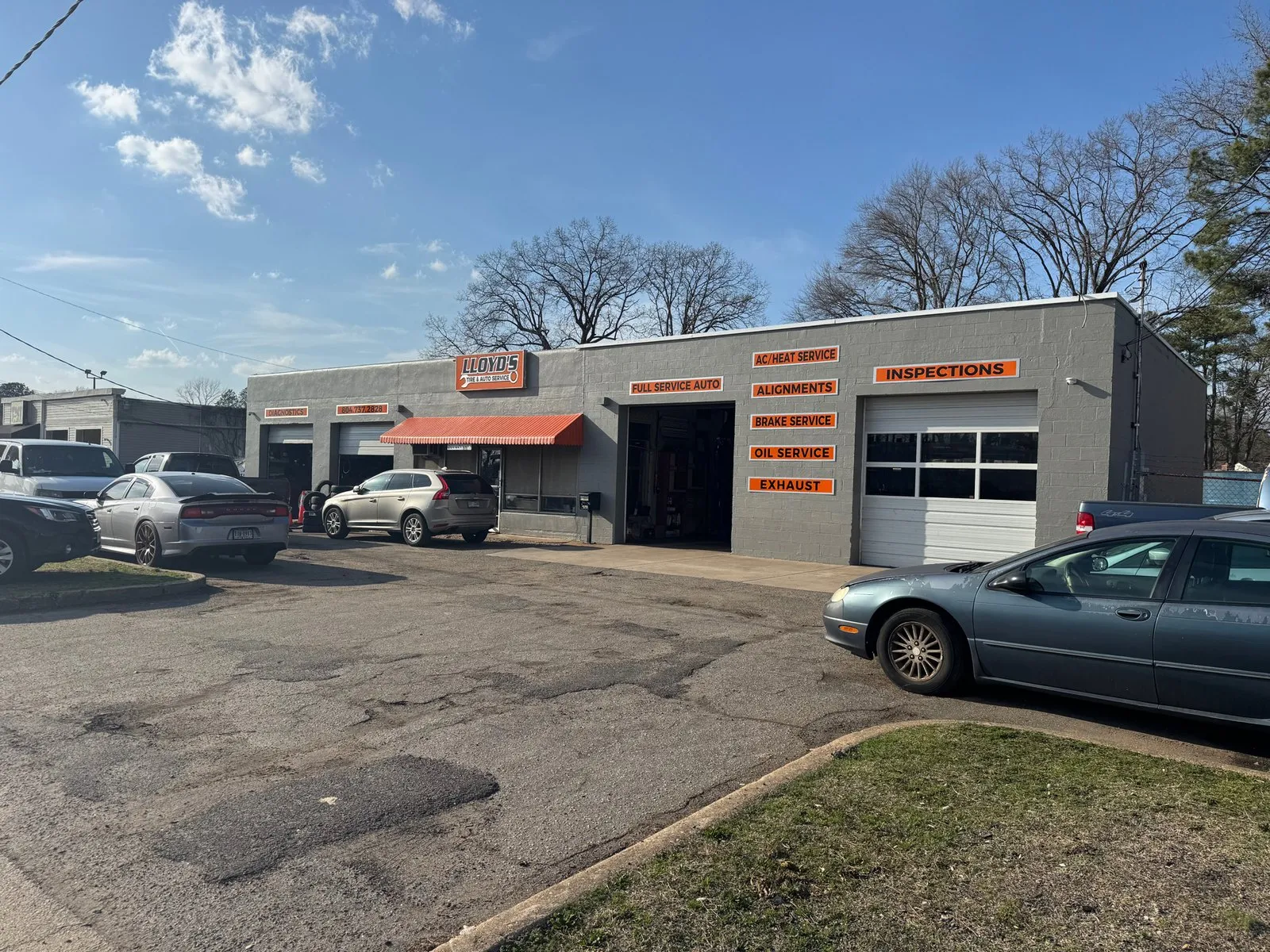The grey block building of Lloyd’s Tire & Auto on West Williamsburg Road, with orange signs listing inspections, alignments, brake service, oil service and exhaust