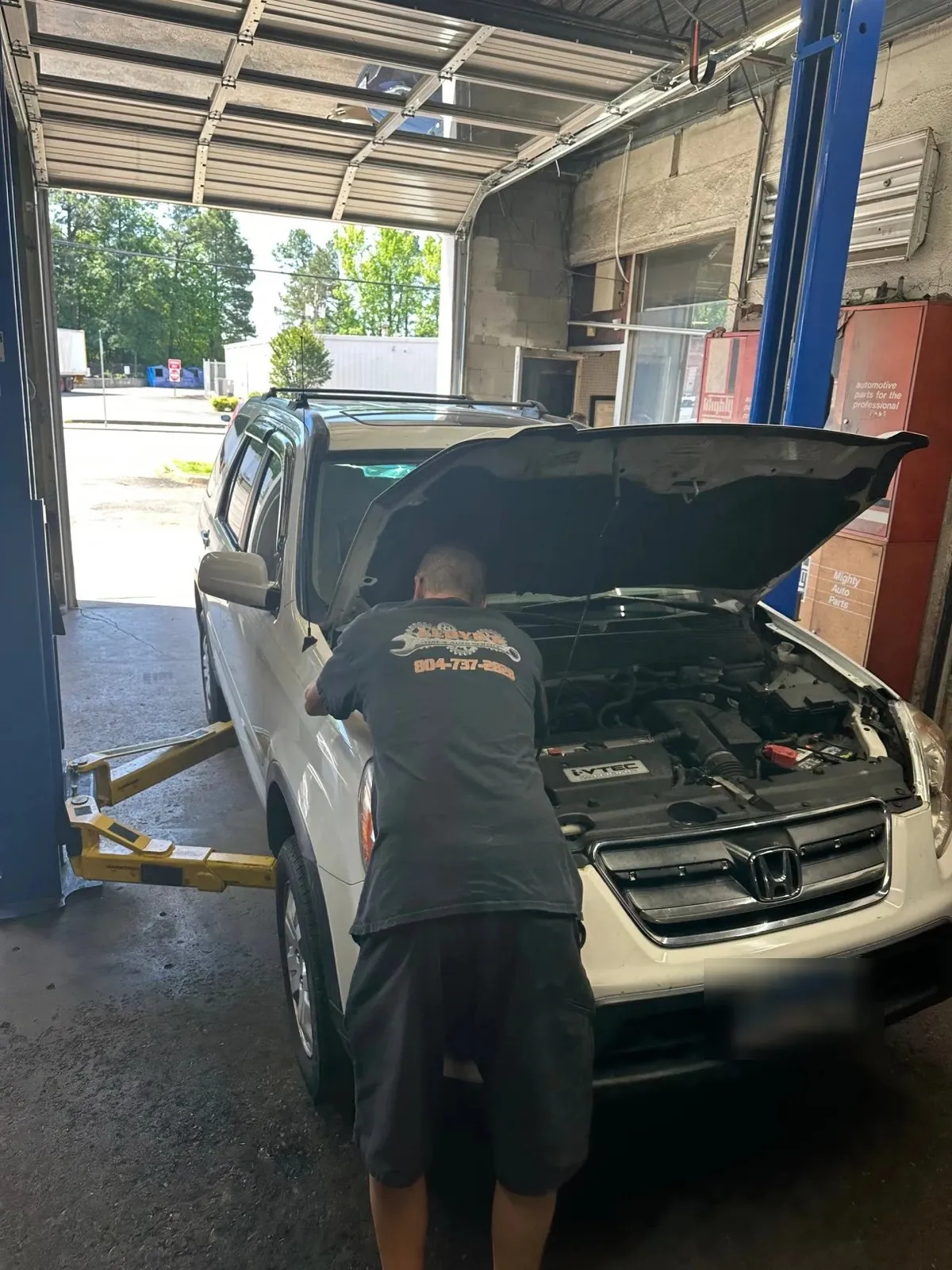 A Lloyd’s technician leaning under the open hood of a white Honda Pilot pulled into the bay